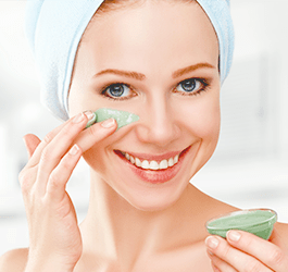 A woman holds a green facial mask, preparing for a skincare routine